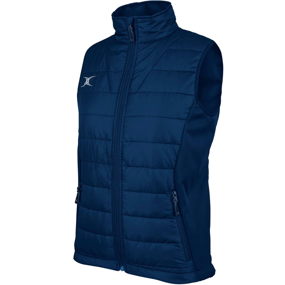 The Gilbert Pro Womens Bodywarmer by Gilbert is a sleeveless, navy blue quilted gilet with a high collar, zippered front and two zippered pockets, featuring a small white logo on the upper left chest.