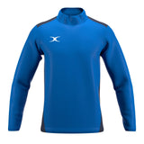 The Gilbert Atom Warm Up Jacket is a blue, long-sleeve athletic jacket with dark side panels, a high collar, and a white Gilbert logo on the left chest. It’s shown on a plain white background.