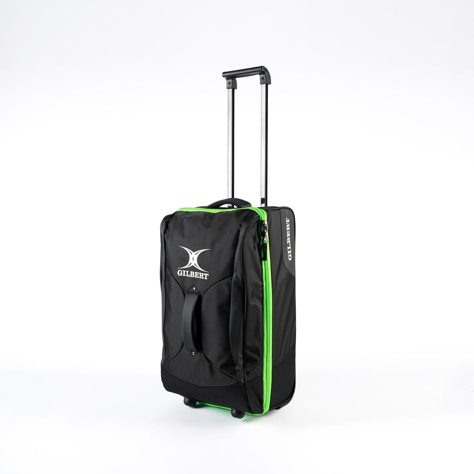 The Gilbert Flight Bag by Gilbert is a black travel bag with green trim, sectioned storage, an extended telescopic handle, front pocket, and two wheels, shown upright on a white background.