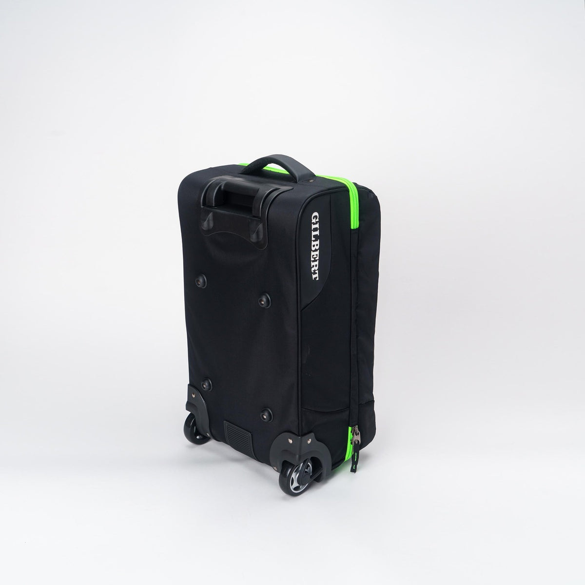 The Gilbert Flight Bag, by Gilbert, is black with green zippers, two wheels, sectioned storage, a top handle, and branding on the side. It is displayed against a plain white background.