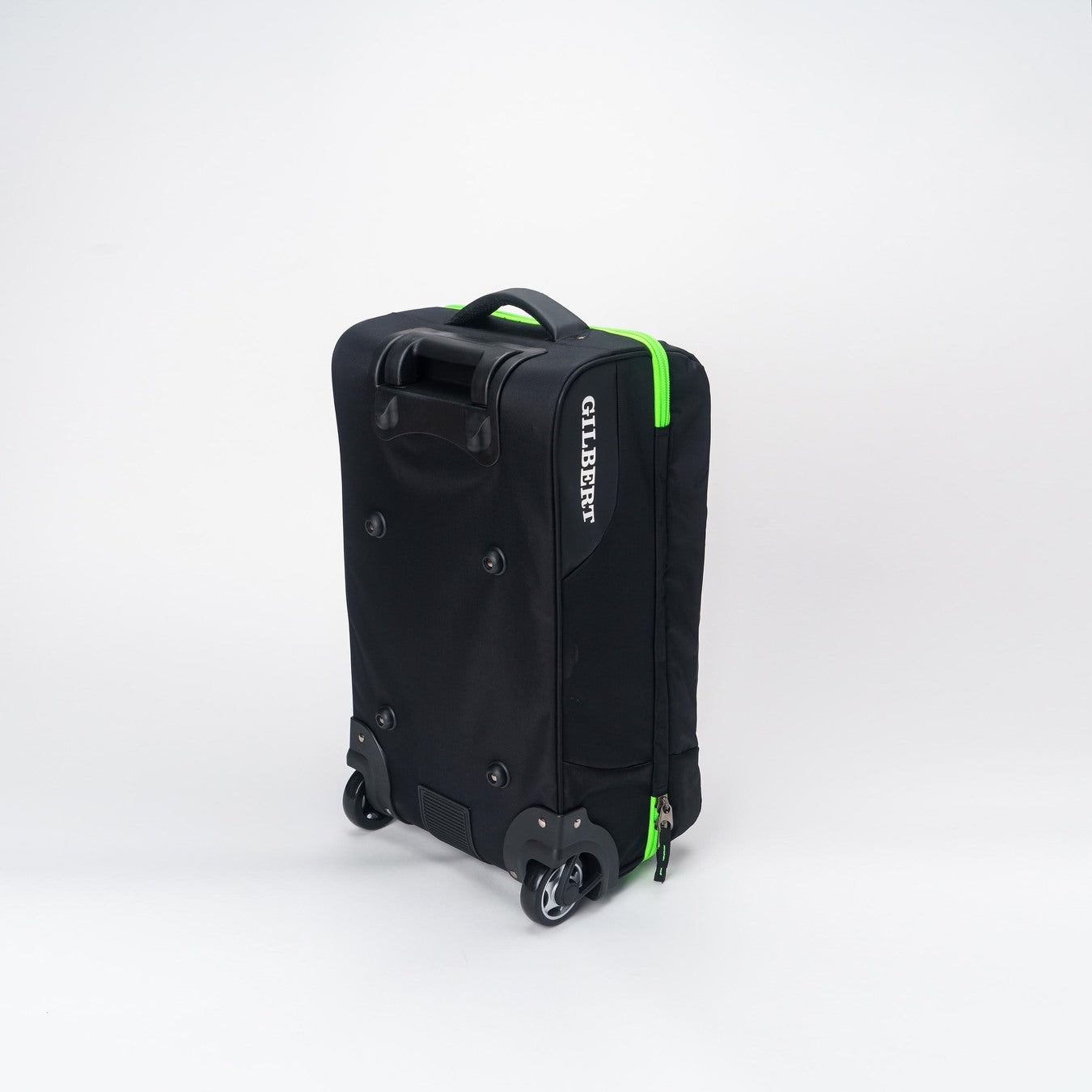 The Gilbert Flight Bag, by Gilbert, is black with green zippers, two wheels, sectioned storage, a top handle, and branding on the side. It is displayed against a plain white background.