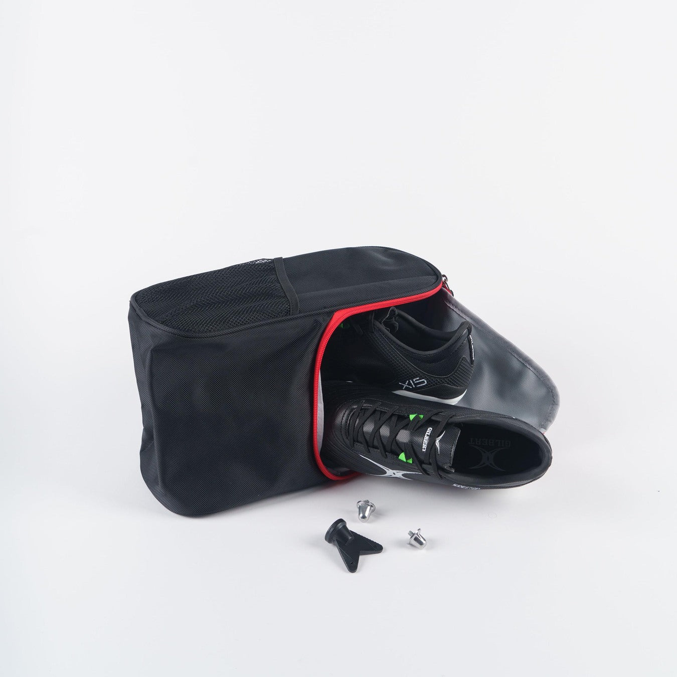 The Gilbert Club V4 Boot Bag by Gilbert, in black with a red zipper, is open to reveal black cycling shoes. Two metal cleats and a screwdriver are displayed in front of the bag on a white background.