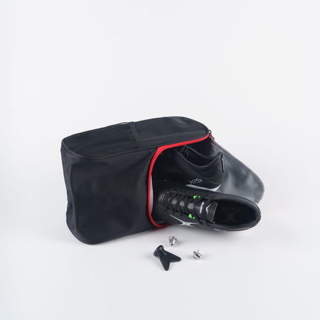 The Gilbert Club V4 Boot Bag by Gilbert, in black with a red zipper, is open to reveal black cycling shoes. Two metal cleats and a screwdriver are displayed in front of the bag on a white background.