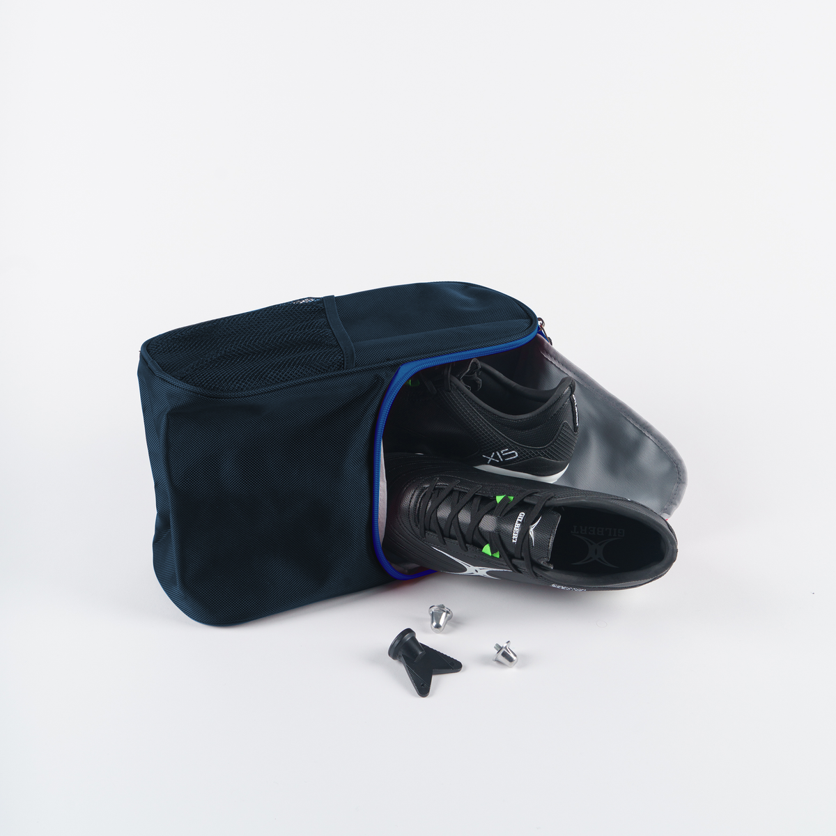 A pair of black sports shoes partly out of a Gilbert Club V4 Boot Bag by Gilbert, with two cleats and a tool, shown on a white background.