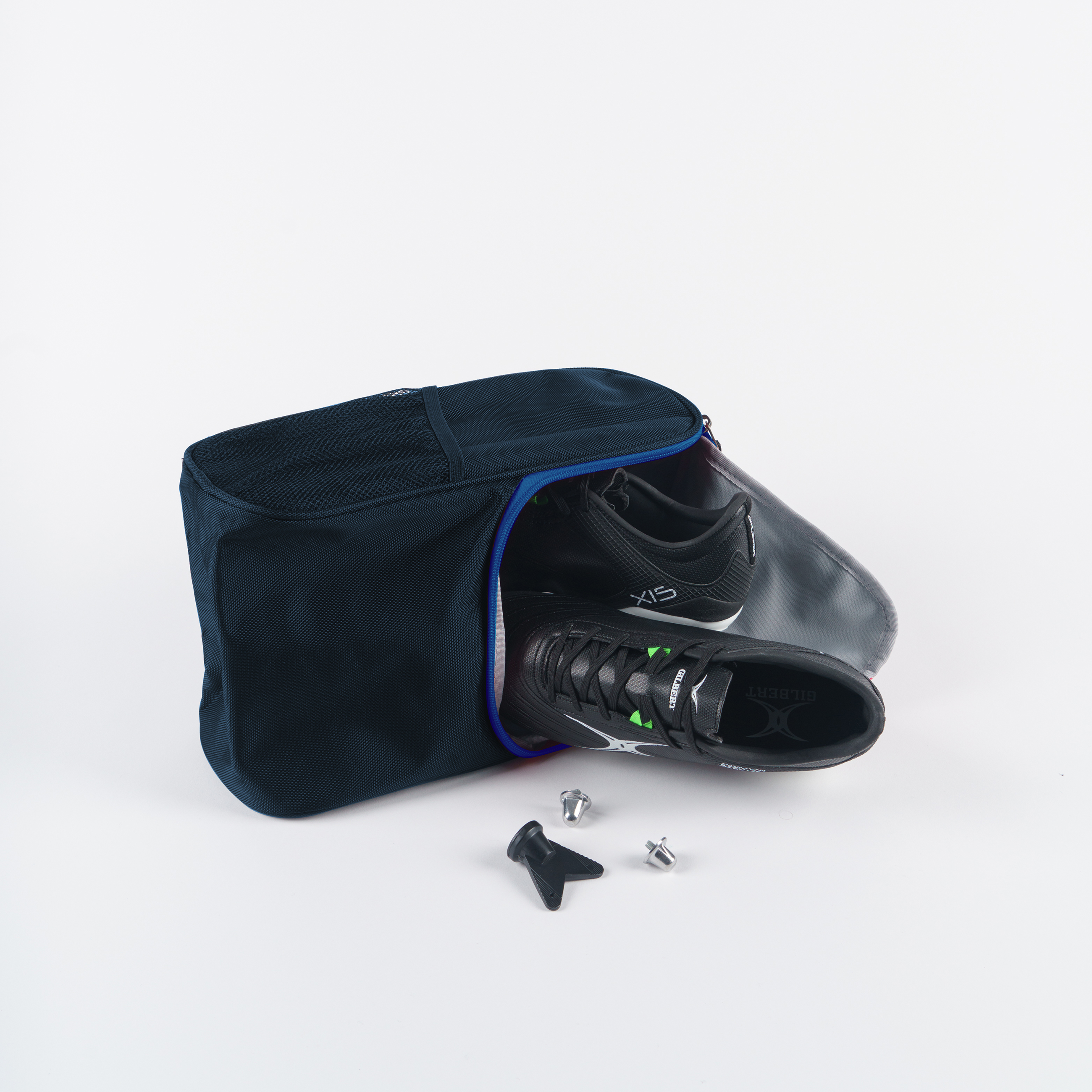 A pair of black sports shoes partly out of a Gilbert Club V4 Boot Bag by Gilbert, with two cleats and a tool, shown on a white background.