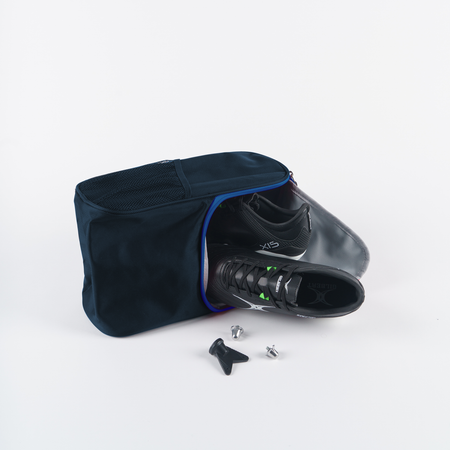 A pair of black sports shoes partly out of a Gilbert Club V4 Boot Bag by Gilbert, with two cleats and a tool, shown on a white background.