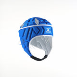 The Gilbert Vapour Junior Headguard by Gilbert, in royal blue with gray padding and chin strap, offers head protection, impact absorption, and ventilation holes. It is displayed against a plain white background.