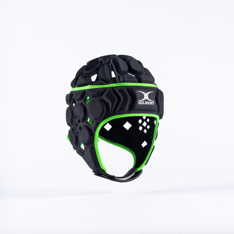 The Gilbert Octane Junior Headguard in black/green features foam protection, ventilation holes, and an expandable lace closure for a secure fit. The padded cap displays the Gilbert logo on the front against a plain white background.
