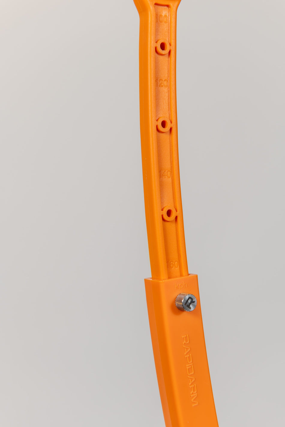 Close-up of a RapidArm+ Ball Thrower by RapidArm, featuring orange plastic with measurement markings, holes, a screw, and the embossed brand name. The adjustable cricket training arm is set against a light plain background.