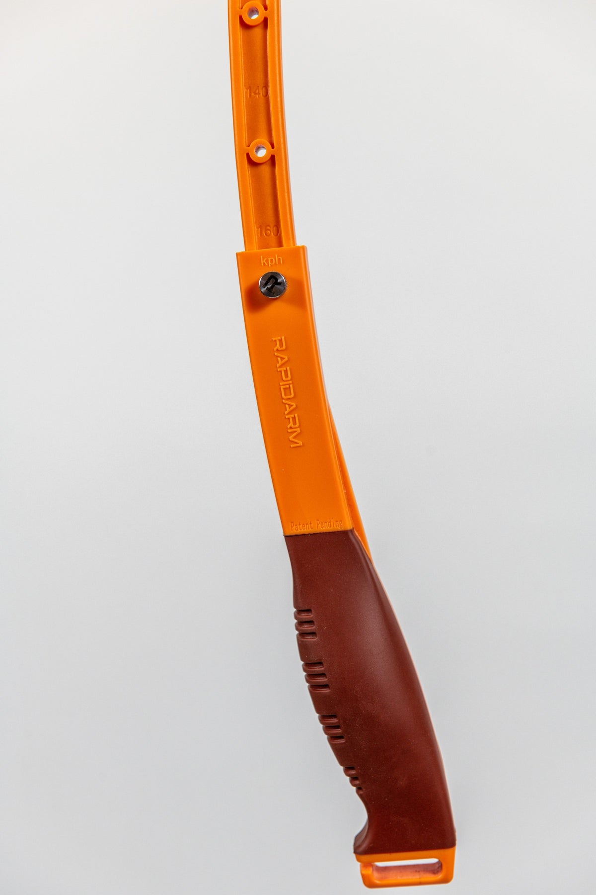 A close-up of the RapidArm+ Ball Thrower by RapidArm, an orange and brown plastic tool with a curved design, adjustable throwing arm, and textured grip handle, shown against a plain light background.