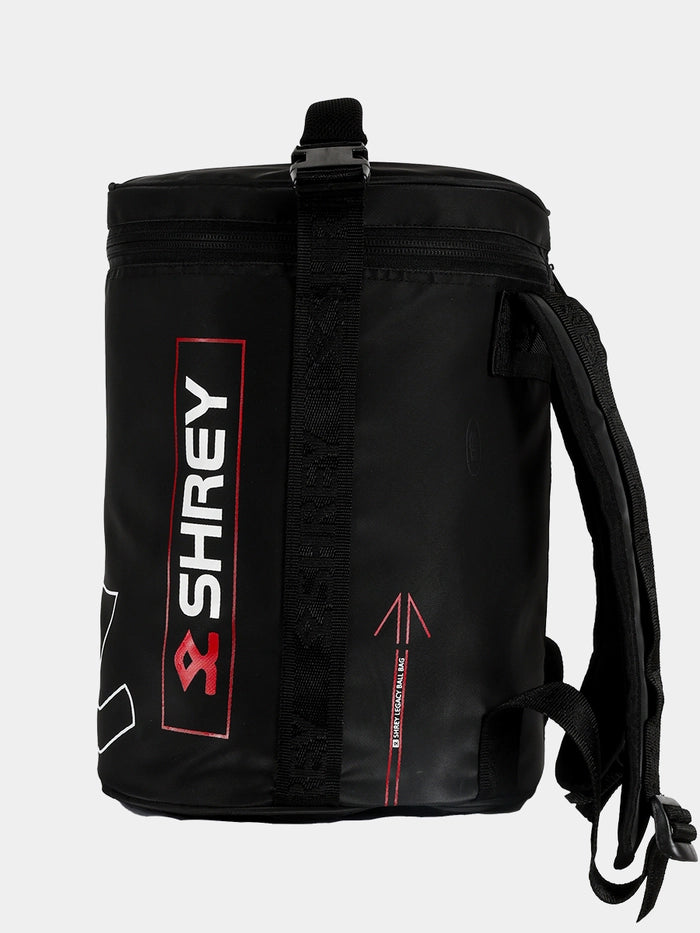 The Shrey Legacy Ball Bag is a black, cylindrical cricket ball bag featuring red details, the Shrey logo, a vertical zipper, top handle, and shoulder straps—perfect for storing training equipment.