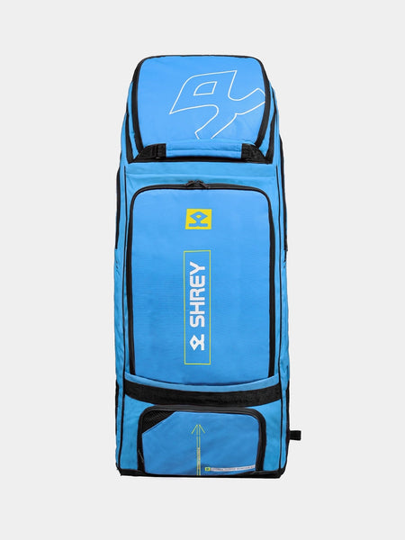The Shrey Legacy Duffle Wheelie 80, a large Brittany Blue cricket bag with black zippers, yellow accents, and multiple compartments, stands upright against a plain background. The Shrey brand and logo are visible on the 80L bag’s front.