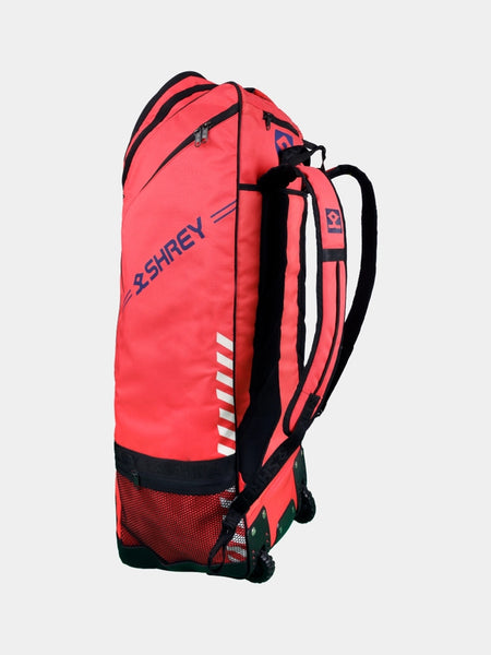 The Shrey Legacy Duffle Wheelie 80 is a spacious red cricket bag with black accents, wheels at the base, multiple zippered compartments, mesh pocket, and padded shoulder straps from Shrey, shown against a plain light background.