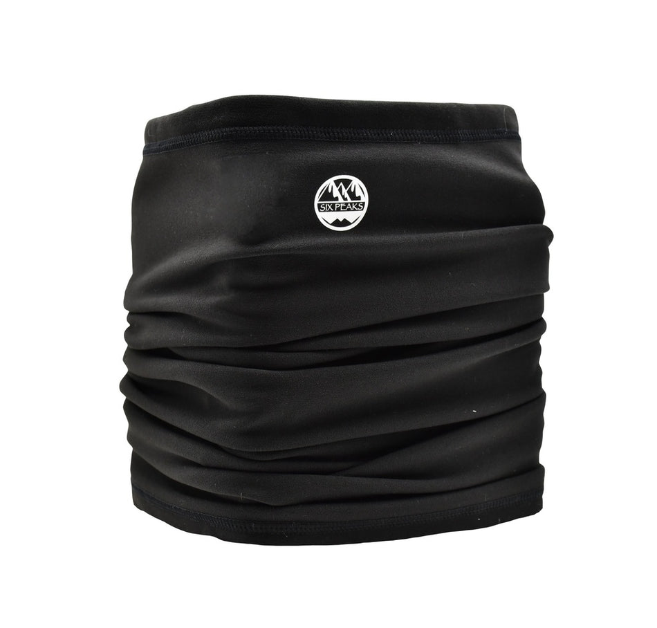 The Six Peaks Winter Neck Warmer is black with a small white mountain logo and "SIX PEAKS" text on the front. Its soft, slightly gathered fabric is wind resistant for added comfort in cold weather.
