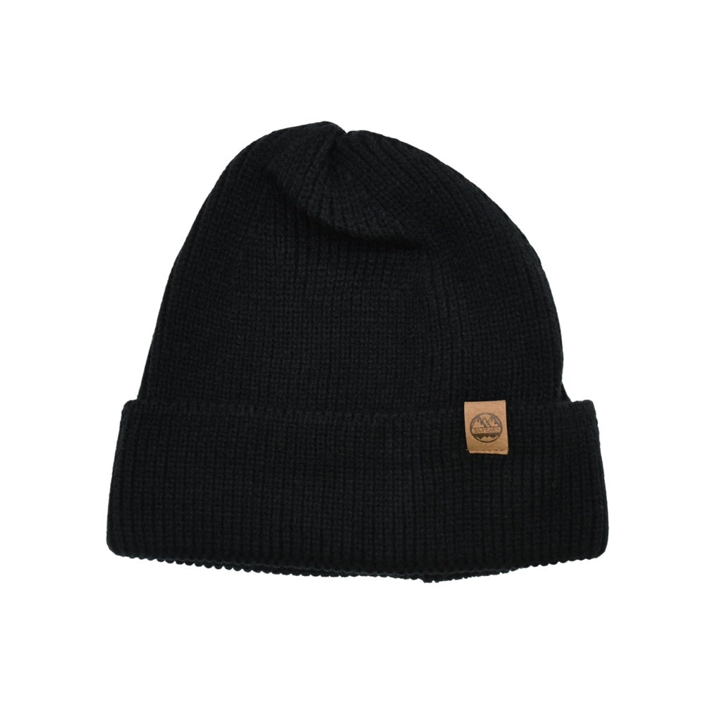 The Six Peaks Beanie by Six Peaks is a black knit winter hat with a folded brim and a small brown leather patch with the logo on the front, shown laid flat on a white background.