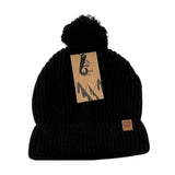 The Six Peaks Pom Beanie in black is a cozy winter hat with a pom-pom, featuring a small brown logo patch on the cuff and an attached brown tag with mountain graphics and the Six Peaks logo.