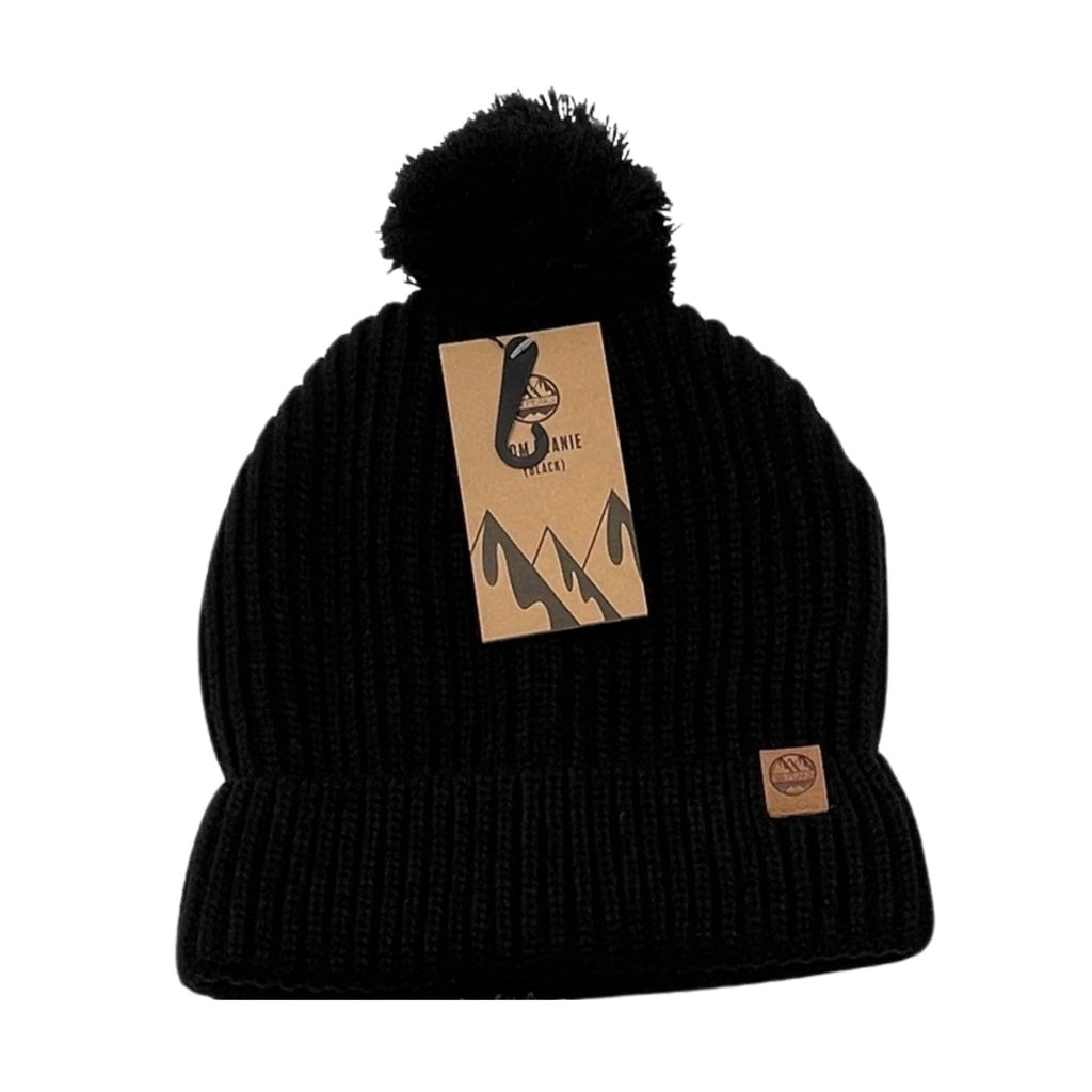 The Six Peaks Pom Beanie in black is a cozy winter hat with a pom-pom, featuring a small brown logo patch on the cuff and an attached brown tag with mountain graphics and the Six Peaks logo.