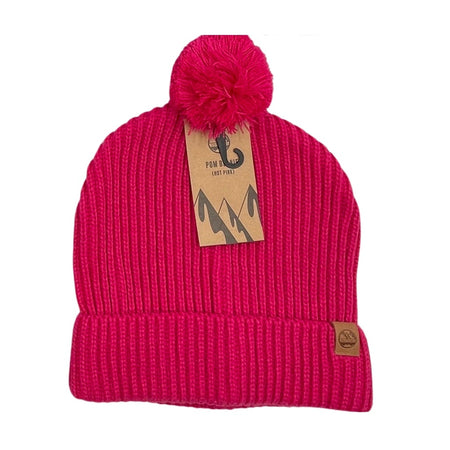 The Six Peaks Pom Beanie is a hot pink winter hat with a pom-pom, folded brim, and two brown tags—one on the cuff and one on top—showcasing mountain graphics and the Six Peaks fishhook logo.
