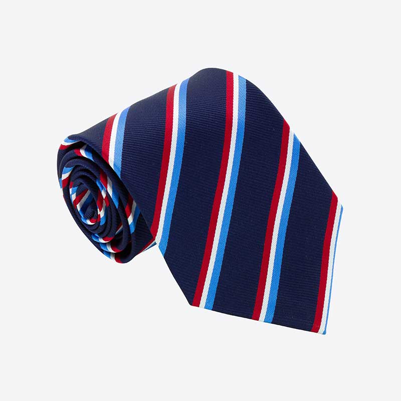 A Custom Club & School Tie by Martin Berrill Sports, rolled up in navy blue with diagonal stripes of light blue, white, and red, displayed on a plain light gray background.