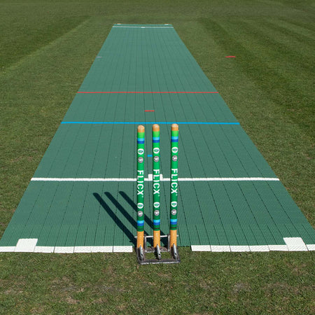 Three cricket stumps stand on the Flicx UK Flicx 2G MAP (Multi Age Pitch) Match Cricket Pitch, featuring white and colored lines on a green mat—perfect for clubs and schools needing versatile pitch setups.