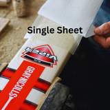 A hand applies a transparent Fibretec Sheet by Gray Nicolls to a Viper Blitz cricket bat on a workbench, providing superior bat protection.