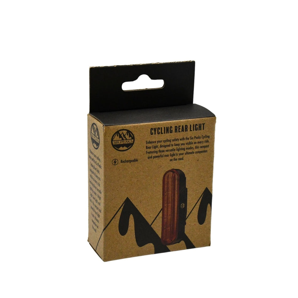 A cardboard box with a black top displays the Six Peaks Cycling Rear Light. Mountain graphics, USB rechargeable icons, and product info decorate the box, with the Six Peaks brand logo near the top left corner.