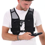 A man wearing a white t-shirt and the black Six Peaks Hydration Running Vest with mesh pockets looks down at a smartphone in his left hand. The background is white.