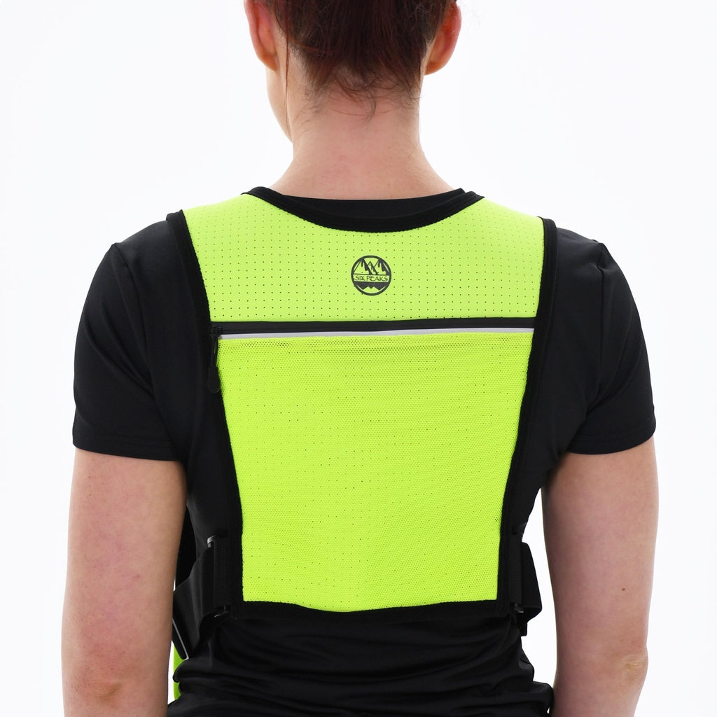 A person wears the Six Peaks Hydration Running Vest in bright yellow-green over a black shirt, shown from the back against a plain white background—ideal for trail running safety.