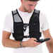A man wearing a white t-shirt and the black Six Peaks Hydration Running Vest with mesh pockets looks down at a smartphone in his left hand. The background is white.