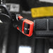 Close-up of a black and red plastic buckle fastened to a black strap with visible stitching on the Six Peaks Junior Cycling Helmet by Six Peaks. A blurred yellow label appears in the background.