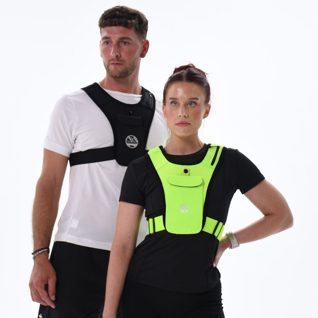 A man and woman wear Six Peaks Running Vests with Phone Holders—a black vest over a white T-shirt for him, a neon green reflective vest over black for her—both from Six Peaks, standing against a plain white background.