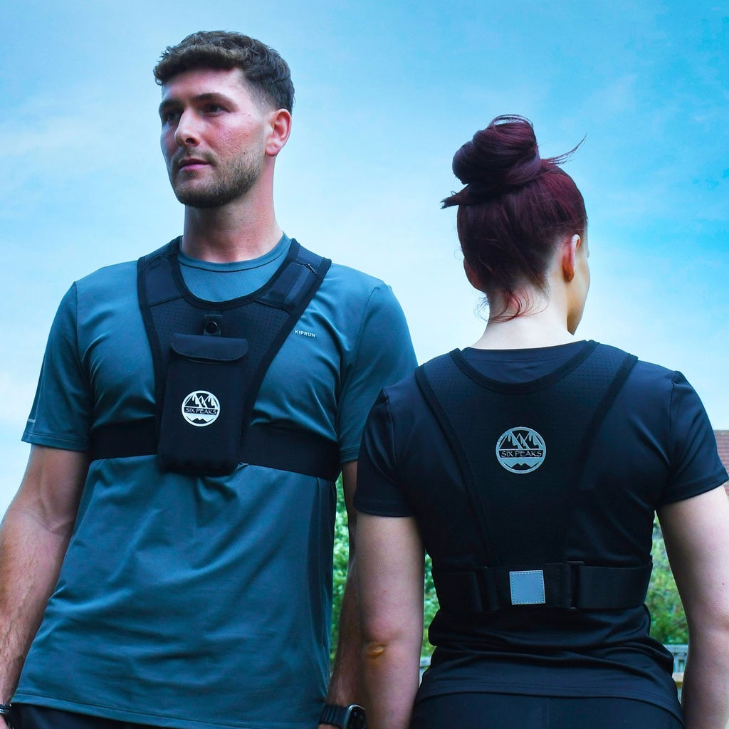 A man and woman outdoors wear Six Peaks Running Vest with Phone Holder; these black vests feature a mountain logo, reflective harnesses for athletic wear, and a handy phone holder, all by Six Peaks.