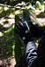 A person wearing Six Peaks Winter Thermal Gloves and a black jacket uses a smartphone outdoors, sitting on a mossy rock in a sunlit forest.