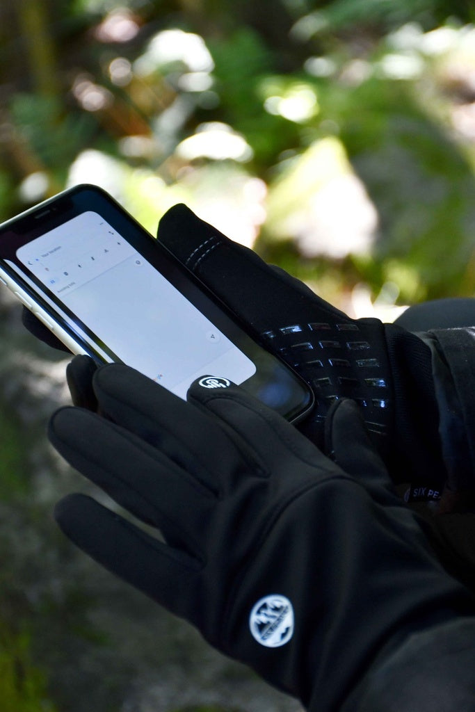 A person wearing Six Peaks Winter Thermal Gloves by Six Peaks uses a smartphone outdoors with a blank note-taking app open, while green foliage is blurred in the background.