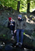 A man and woman wearing Six Peaks jackets and Six Peaks LED Lighted Beanie Hats sit on rocks by a forest stream, smiling at each other as sunlight streams through the trees, creating a peaceful, nature-filled scene.