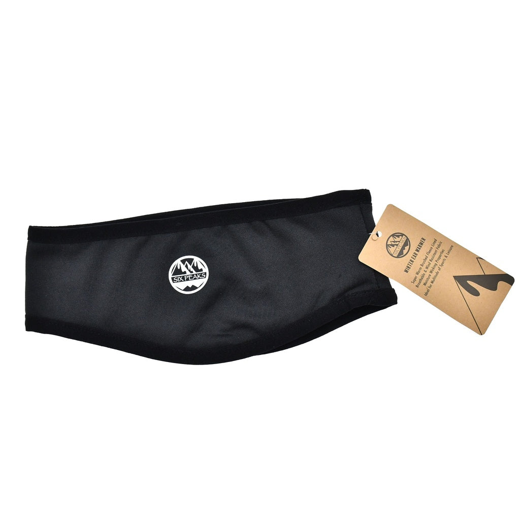 The Six Peaks Winter Ear Warmer is black, fleece lined, and wind resistant. It has a white mountain logo centered on the front and a brown Six Peaks tag with branding and care instructions for cozy winter wear.