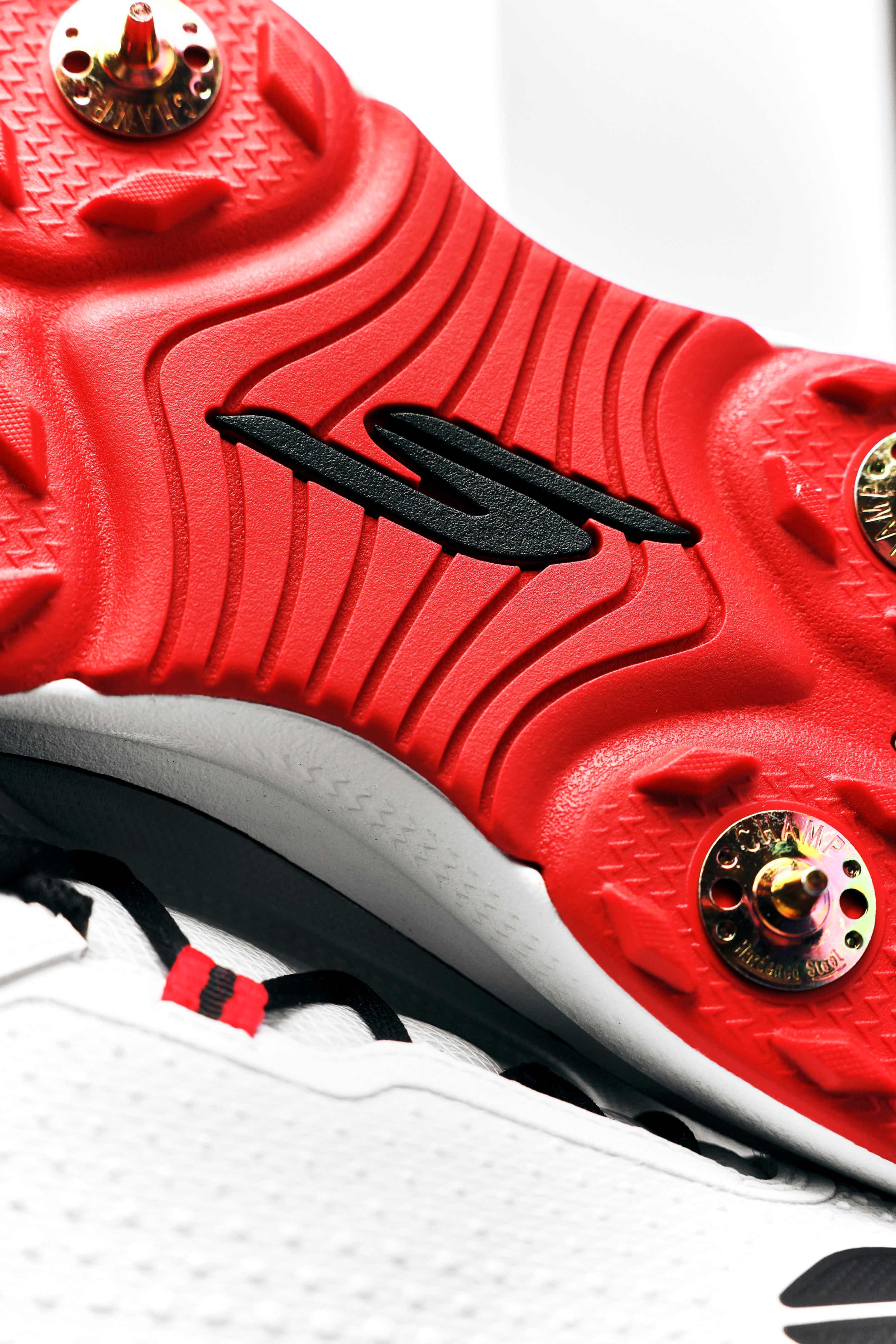 Close-up of the red sole of the Skechers Cricket Elite Cricket Shoe by Skechers, showing textured grooves, gold studs, a central black logo, and Arch Fit insole. The partially visible upper is white with black and red accents.