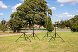 Four Ritelite Sports Lite Portable Floodlights stand on a grassy field with trees, a fence, and houses in the background under a blue sky with scattered clouds.