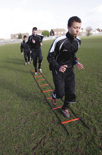 Three young athletes in black sportswear run through the Precision Speed Ladder by Precision Training, practicing footwork drills on a grassy field with houses in the background.