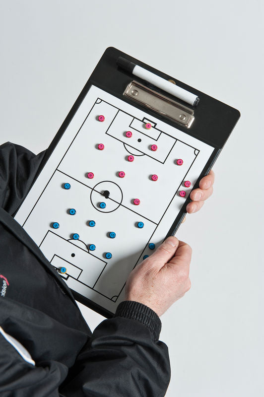 A person holds the Precision Training Precision Soccer Coaches Double-Sided Clipboard, showing player positions with pink and blue magnets on a soccer pitch board and a dry-wipe marker clipped at the top.