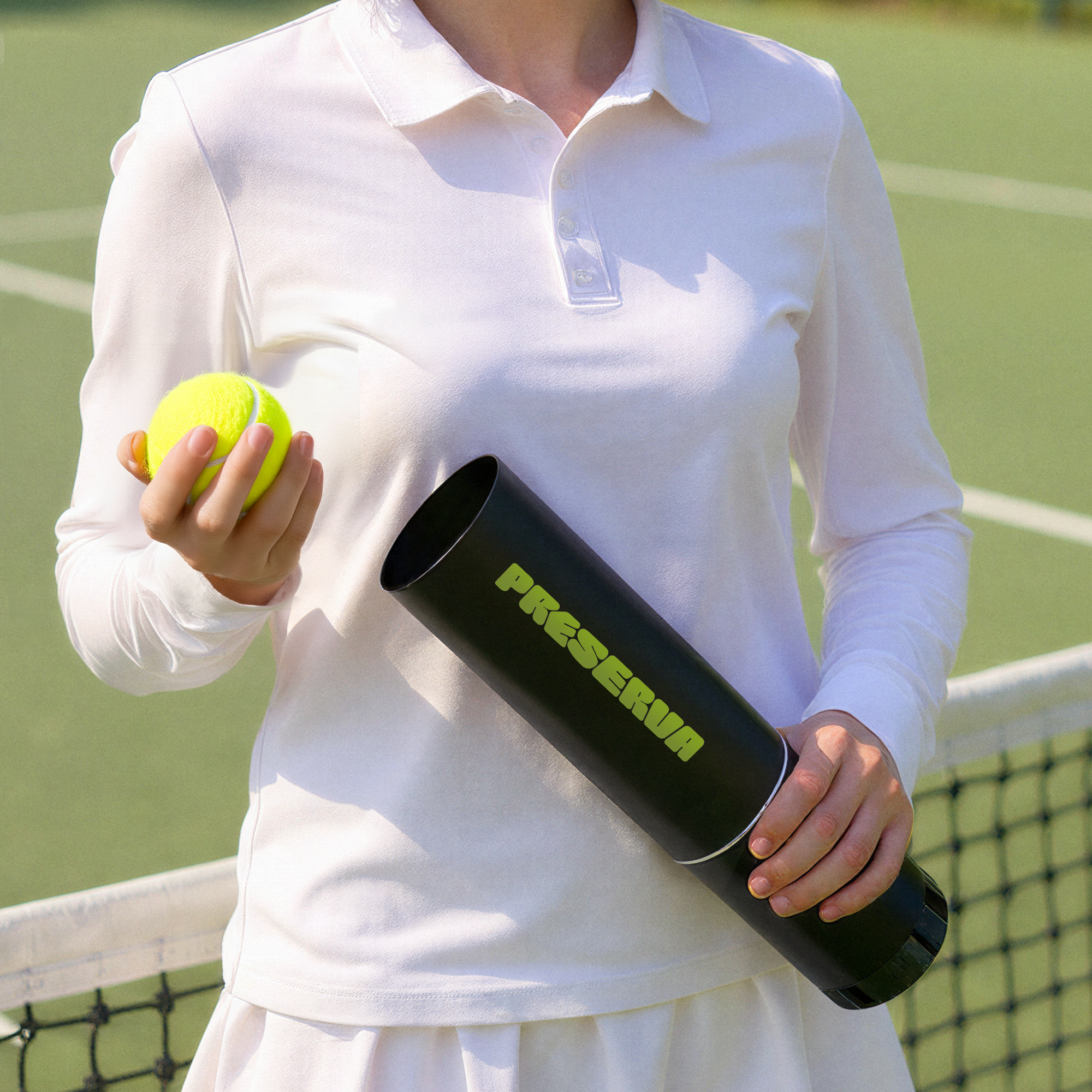 A person in a white tennis outfit, holding a tennis ball and the Preserva Rechargeable Tennis Ball Pressuriser by Preserva, stands by a tennis net on an outdoor court.