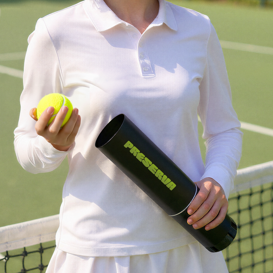 A person in a white tennis outfit, holding a tennis ball and the Preserva Rechargeable Tennis Ball Pressuriser by Preserva, stands by a tennis net on an outdoor court.