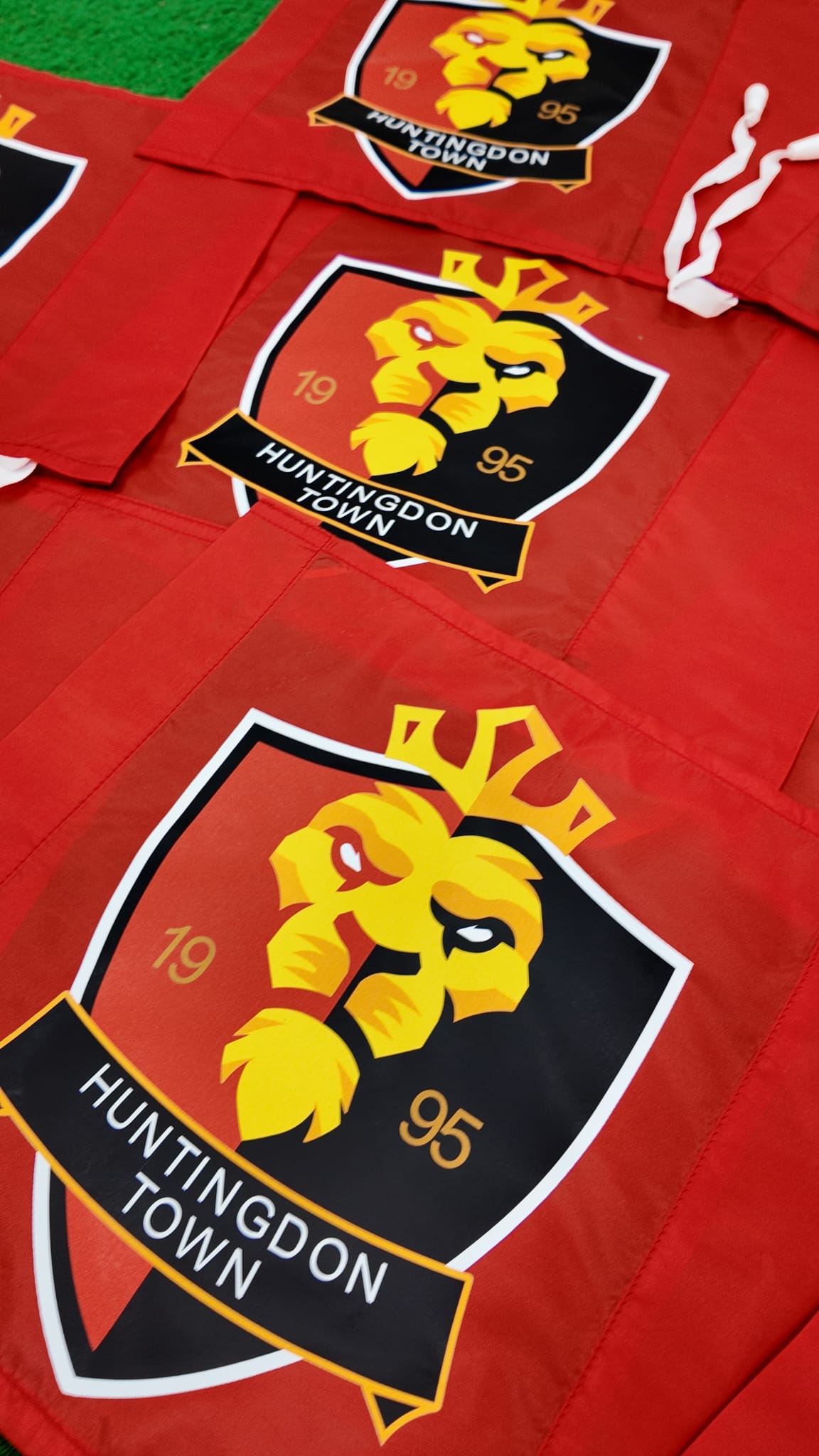 A close-up of Custom Printed Corner Post Flags (Single Colour Flag & Logo) by Martin Berrill Sports, featuring a black, gold, and yellow lion crest reading HUNTINGDON TOWN and 1995. Ideal for club branding or use at sporting events.