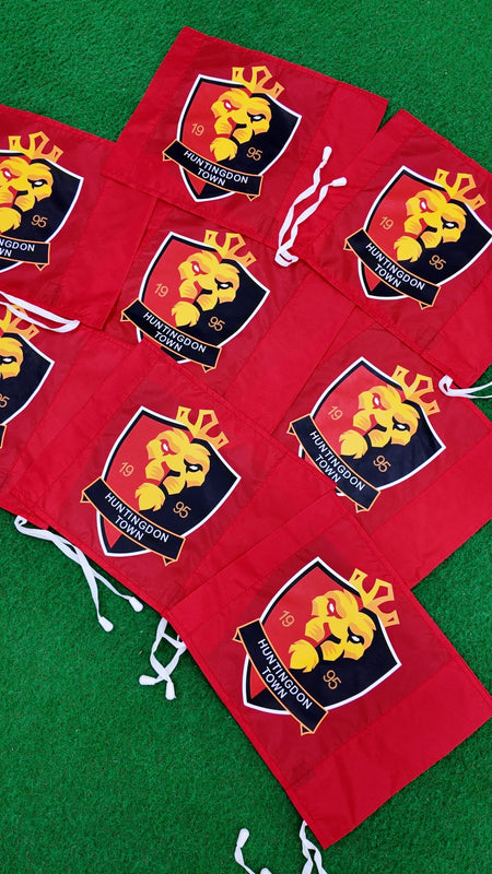 Custom Printed Corner Post Flags (Single Colour Flag & Logo) by Martin Berrill Sports featuring a crowned lion logo, "HUNTINGDON TOWN FC," and 1985 on red fabric with white tie strings—ideal for corner post or branded flag posts.