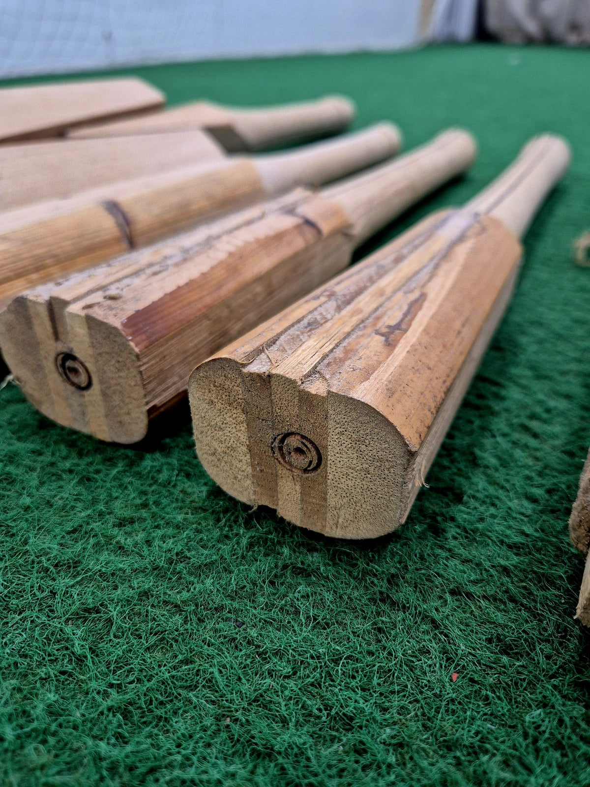 Close-up of several bamboo cricket bats on green turf highlights the natural grain at the bat ends—ideal for showcasing Martin Berrill Sports Cricket Bat Rehandle craftsmanship.