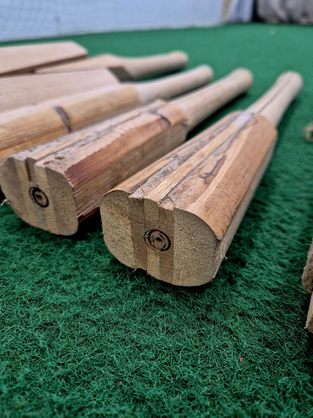 Close-up of several bamboo cricket bats on green turf highlights the natural grain at the bat ends—ideal for showcasing Martin Berrill Sports Cricket Bat Rehandle craftsmanship.