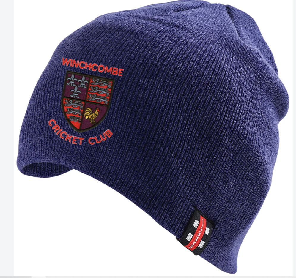 The Winchcombe CC Beanie Hat by Gray Nicolls is a dark blue knit with the club logo—lions, fleur-de-lis, and "Winchcombe Cricket Club" in red and orange—plus a small black and red stitched tag on the brim.