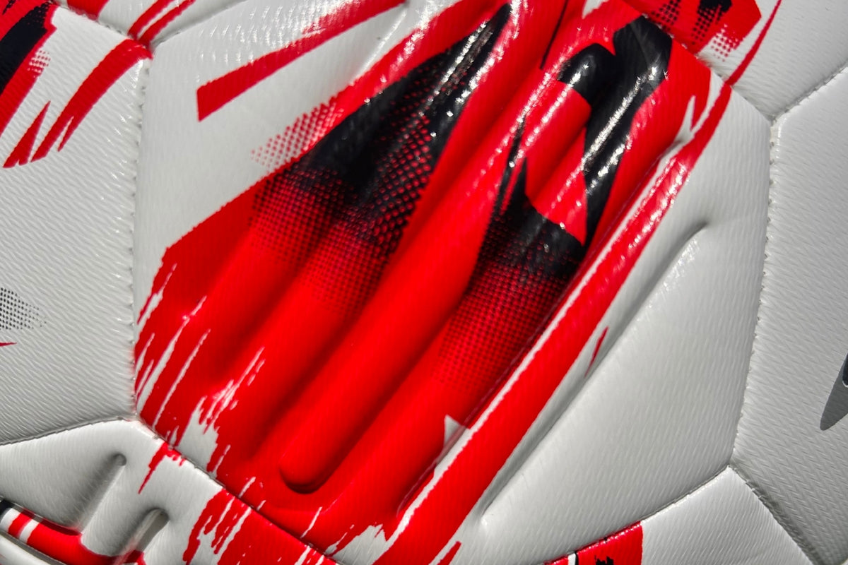 A close-up of the Samba Infiniti Max Training Ball by Samba Sports—a white soccer ball with red and black abstract patterns, featuring textured panels and precision-moulded grooves for enhanced control—perfect for training sessions and utilizing advanced AIRFOAM Technology.