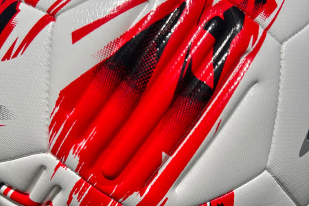 A close-up of the Samba Infiniti Max Training Ball by Samba Sports—a white soccer ball with red and black abstract patterns, featuring textured panels and precision-moulded grooves for enhanced control—perfect for training sessions and utilizing advanced AIRFOAM Technology.