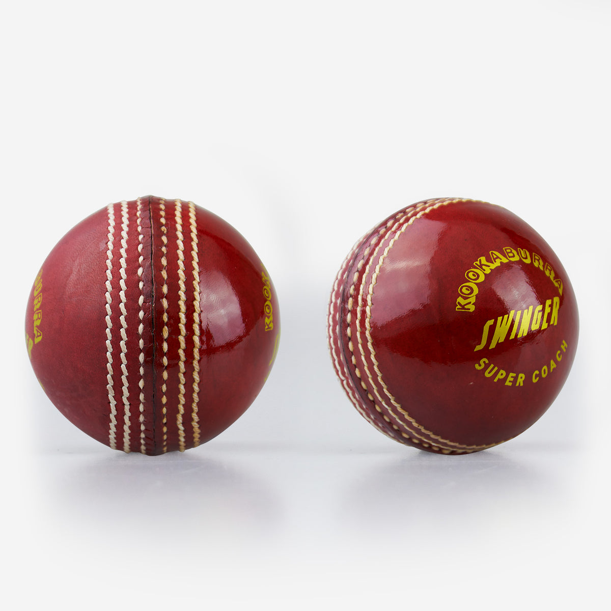 Two shiny red Kookaburra Super Coach Swinger leather cricket balls with white stitching—one shows the seam, while the other displays Kookaburra branding—ideal for swing training on a plain white background.